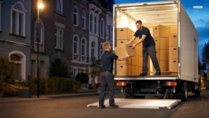 Zwei Umzugshelfer übergeben am Abend an der Ladebordwand eines LKW einen Umzugskarton, im Laderaum gestapelte Kartons (KI-generiertes Bild)