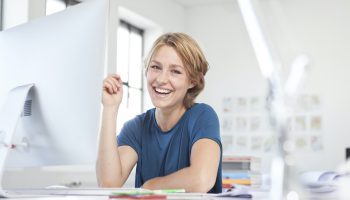 Portrait of happy young woman at her desk in a creative office